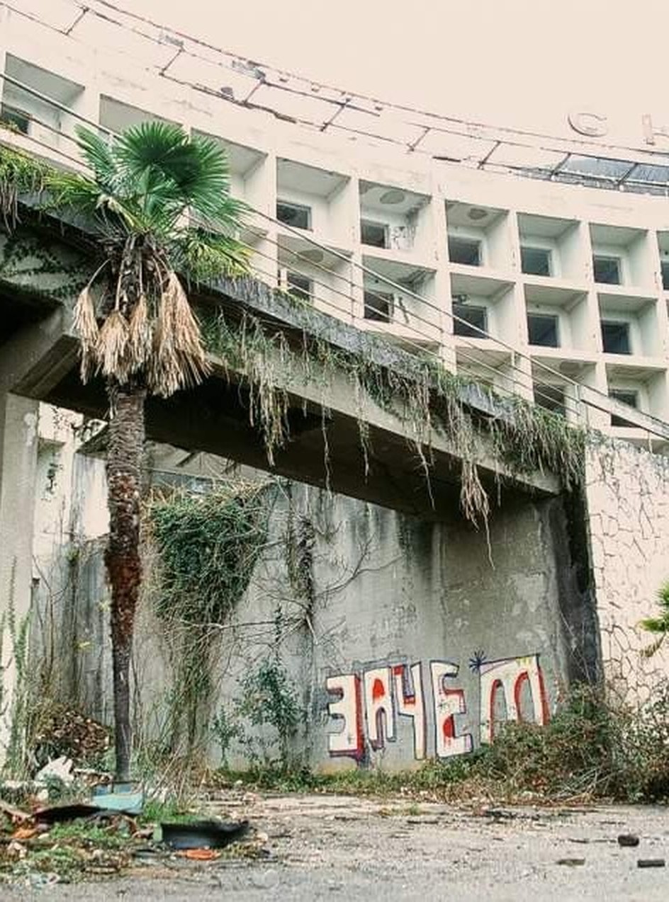 An abandoned sanatorium with the word “ЗАЧЕМ” — “what for” — painted across the concrete below the balconies.